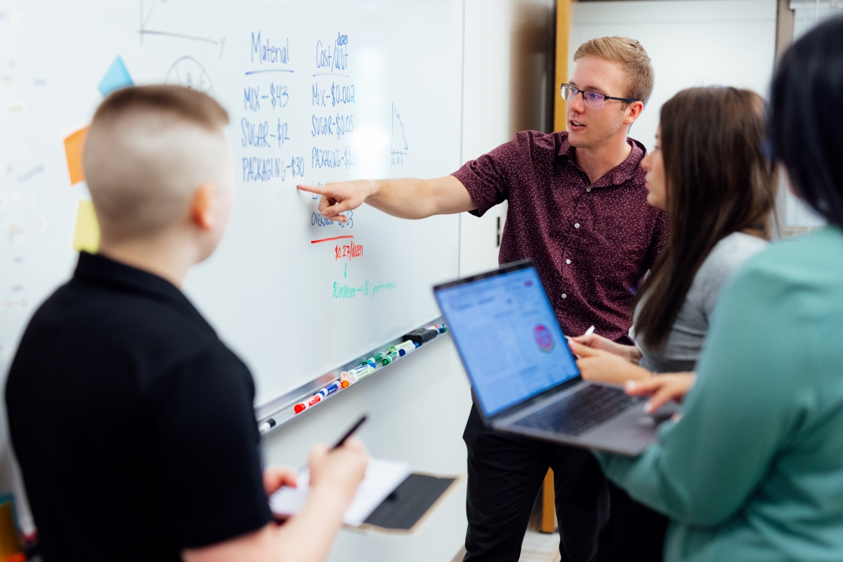 Man pointing on white board as students watch